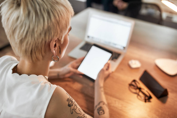 Modern business woman. Young tattooed woman with short haircut using digital tablet while sitting at her workplace. Business woman at work - Φωτογραφία, εικόνα