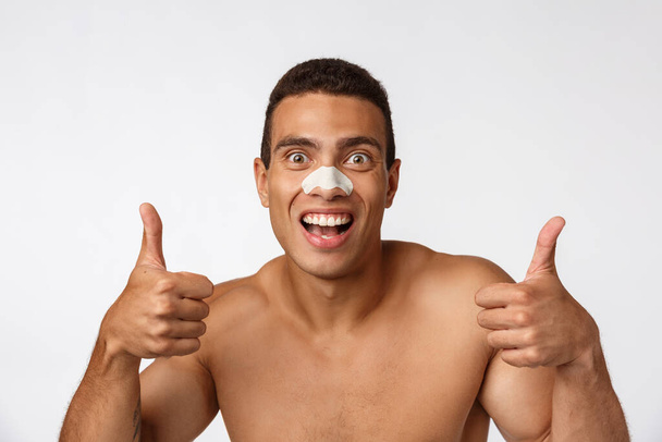 Komea afrikkalainen amerikkalainen mies käyttää nenä laastari vähentää mustia pisteitä ja ryppyjä, käyttää suihku lippis, hymyilee laajasti
. - Valokuva, kuva
