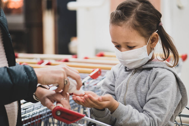 A criança na máscara protetora faz a desinfecção de mãos com o desinfetante no supermercado
. - Foto, Imagem