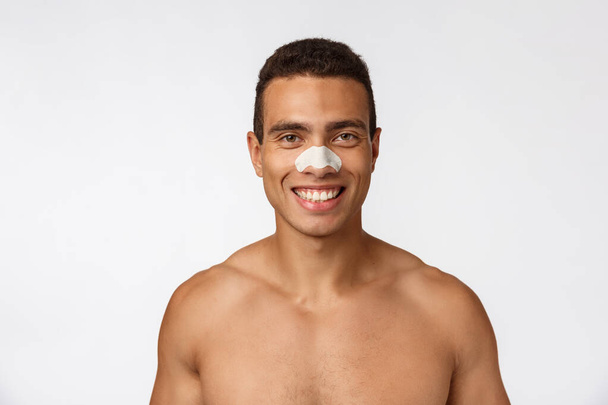 Hezký africký Američan používá nos náplast pro snížení černé tečky a vrásky, nosí sprchový čepice, usmívá široce. - Fotografie, Obrázek