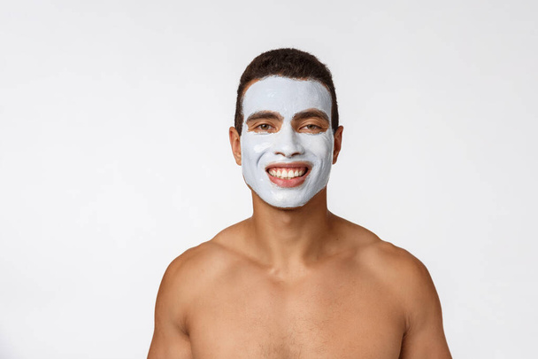Picture of cheerful nice young african guy smiling on camera. Portrait of man with cream mask on cheeks. Beauty routine - Photo, Image