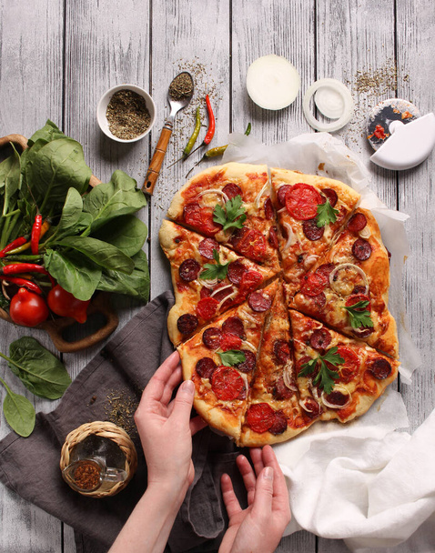 Italian cuisine. Pizza with sausages on a wooden background, background image, copy space, pizza with hands - Фото, изображение