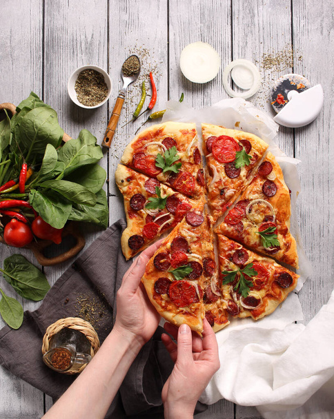 Italian cuisine. Pizza with sausages on a wooden background, background image, copy space, pizza with hands - Fotó, kép