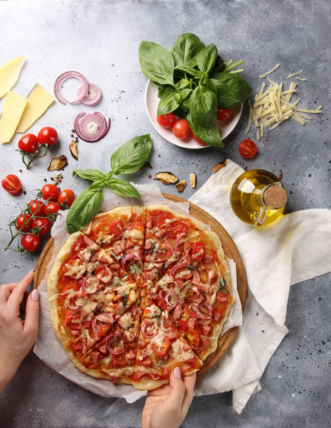 Italian cuisine. Pizza on a white and gray background. Cooking process. Fresh vegetables and basil. background image, copy space, pizza with hands - Photo, Image