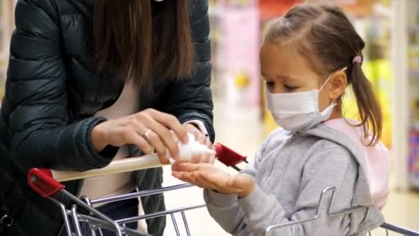 Kind in beschermend masker maakt desinfectie van handen met ontsmettingsmiddel bij kruidenier. - Video