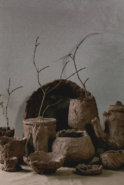 Groupe de vases artisanaux en argile brute et plats avec branches sèches à l'intérieur sur la table avec nappe en lin et mur gris derrière
. - Photo, image