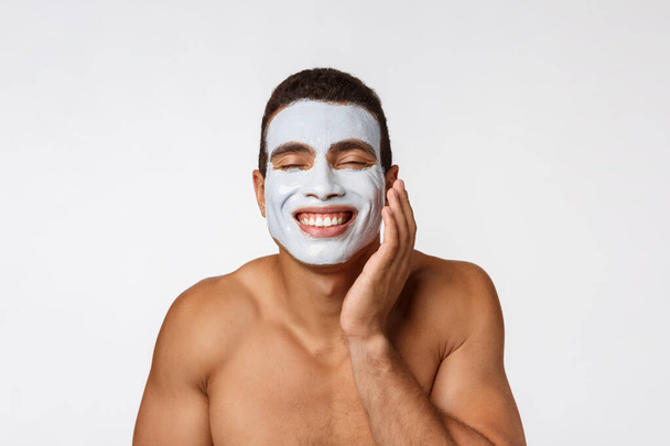 Picture of cheerful nice young african guy smiling on camera. Portrait of man with cream mask on cheeks. Beauty routine - Fotó, kép