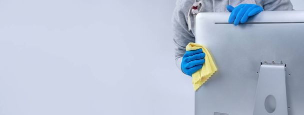 Young woman housekeeper in apron is cleaning silver computer surface with blue gloves, wet yellow rag, close up, copy space, blank design concept. - Photo, Image