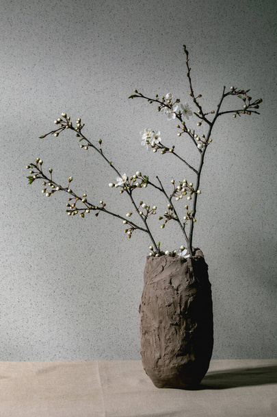 Blossom cherry branches in craft clay vase on grey table cloth. Spring interior decorations. - Foto, Bild