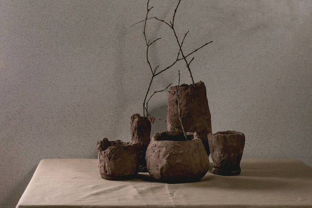 Groupe de vases artisanaux en argile brute avec branches sèches à l'intérieur sur table avec nappe en lin et mur gris derrière. - Photo, image