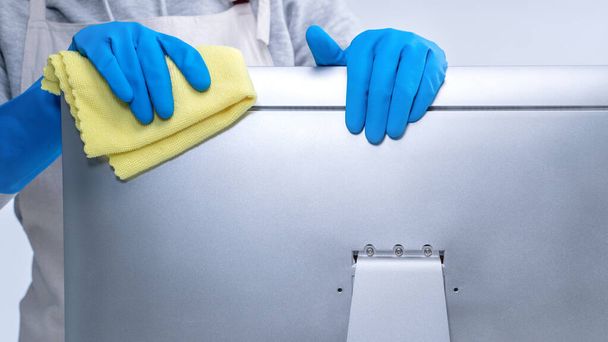 Young woman housekeeper in apron is cleaning silver computer surface with blue gloves, wet yellow rag, close up, copy space, blank design concept. - Фото, зображення