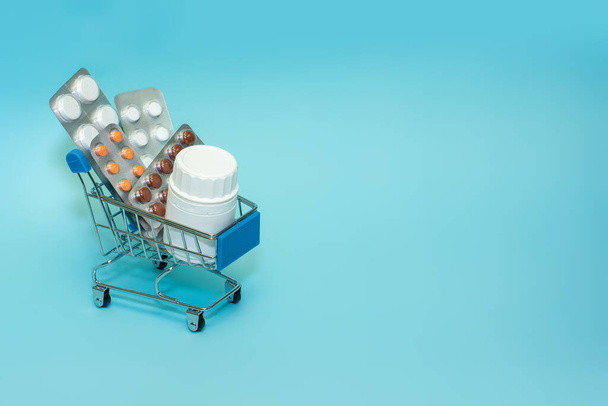 Winkelwagen met pillen op een blauwe achtergrond. Het concept van de geneeskunde van online winkelen. Kopieer ruimte voor tekst - Foto, afbeelding