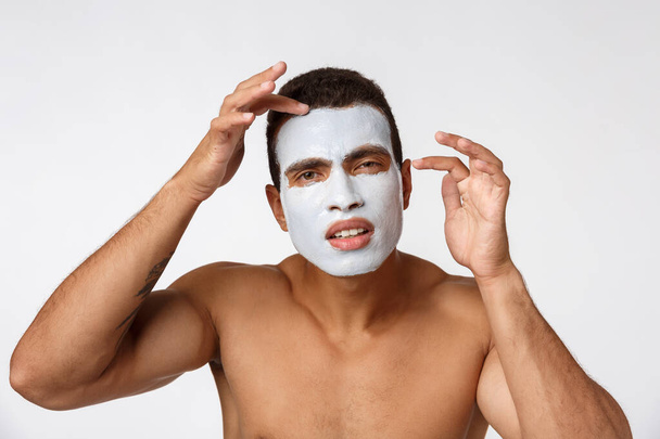 Foto de hombre afroamericano sin camisa sonriendo y aplicando crema facial aislada sobre fondo blanco
 - Foto, Imagen