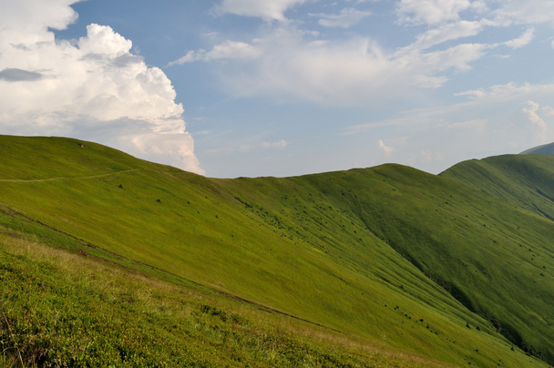 hegyi ridge lejtők borított zöld fű és a felhős kék ég - Fotó, kép