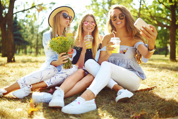 Tres chicas jóvenes de moda se ríen y hacen selfies en el caluroso día de verano. Los amigos disfrutan de sus vacaciones juntos. Concepto de verano
. - Foto, imagen