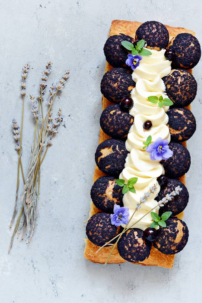 Dessert Saint Onore. Berry pie. Puff pastry tart with profiteroles, butter cream, black currant jam with fresh mint, lavender flowers and berries. Gourmet french dessert on gray background. - Photo, Image