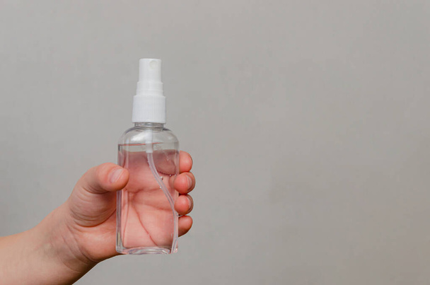 Hands of a child of four years holding a bottle with a sanitizer on a gray background. Sanitary precautions - hand disinfection. - Zdjęcie, obraz