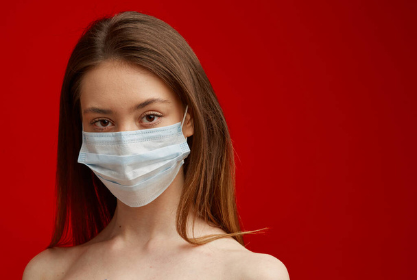 A young girl in a medical mask on a red background. Poster about the coronavirus COVID-19 pandemic. - Fotó, kép