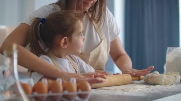Medium shot of mother and daughter rolling dough in kitchen. Mom teaches daughter to cook dough. Girl learns to cook pastries. Kneading the dough together. Roll out the dough for baking. - Footage, Video
