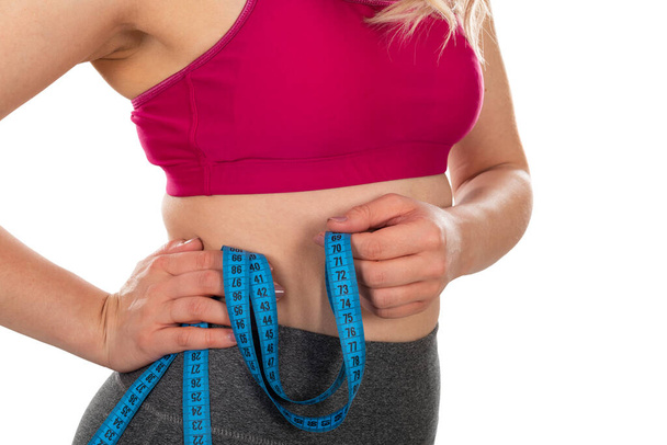 Young females waistline, holding a measuring tape on isolated background - weight loss, diet, body shaping concept - Photo, Image