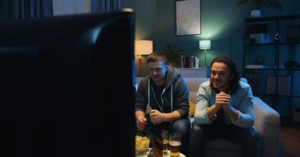 Handsome Caucasian men friends sitting on sofa and worrying for football team in match while watching sport channel on TV. Scoring goal concept. - Filmagem, Vídeo