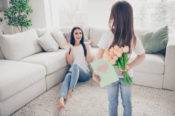 Photo of pretty little girl young charming brunette mommy waiting 8 march present girl hiding postcard tulips flowers positive affectionate emotions sitting floor home indoors - Fotografie, Obrázek