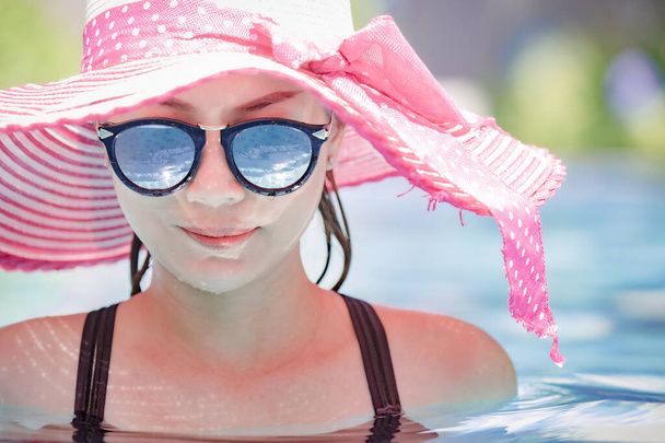 Portrait of 40s adult Asian woman wear sunglasses and put on big hat standing in pool and looking to water with reflection in lens glass. Process in soft film style. - Foto, imagen