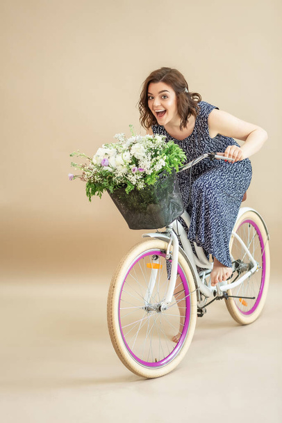 Hermosa mujer joven en bicicleta sobre fondo beige. chica emocional aprendiendo a andar en bicicleta. miedo de subirse a la bicicleta
. - Foto, imagen