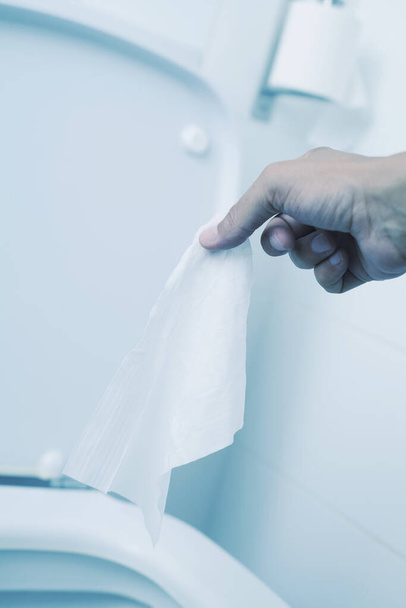 Κοντινό πλάνο ενός νεαρού καυκάσιου που ετοιμάζεται να πετάξει ένα υγρό μαντηλάκι στην τουαλέτα, σε μια λευκή τουαλέτα με πλακάκια. - Φωτογραφία, εικόνα