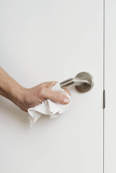 close-up de um homem caucasiano que abre uma porta cobrindo a maçaneta com uma toalhita desinfectante, como medida para evitar a transmissão de infecções
 - Foto, Imagem