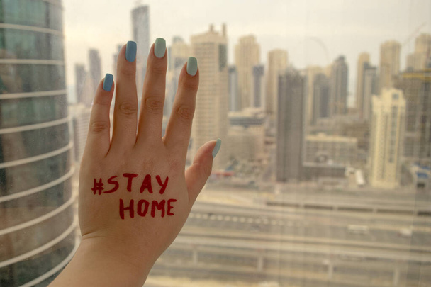 Vrouw hand op een raam met "Stay Home" schrijven op een wazig Dubai wolkenkrabbers achtergrond. Blijf thuis tijdens COVID-19 uitbraak. - Foto, afbeelding