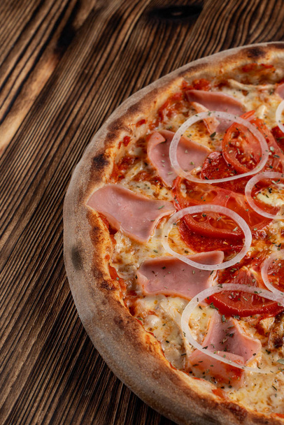 Close up of classic italian pizza with ham, onion rings and tomato, vertical, half of pizza - Photo, Image
