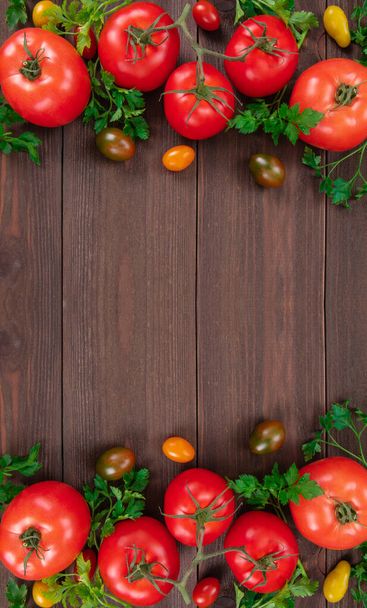 Red tomatoes, cherry tomatoes and parsley leaves arranged in vertical side frame on wooden background, top view, space for text - Photo, Image