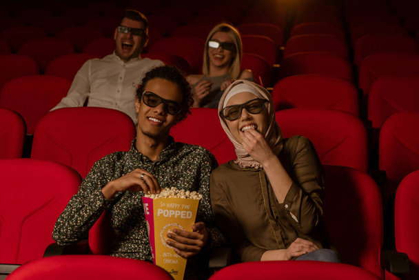 African american muslim man with his wife sitting in movie theater, watching 3D movie, eating popcorn, smiling. - Foto, immagini