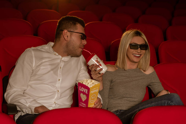 Happy couple sitting in movie theater, watching 3D movie, eating popcorn, smiling - Foto, Bild