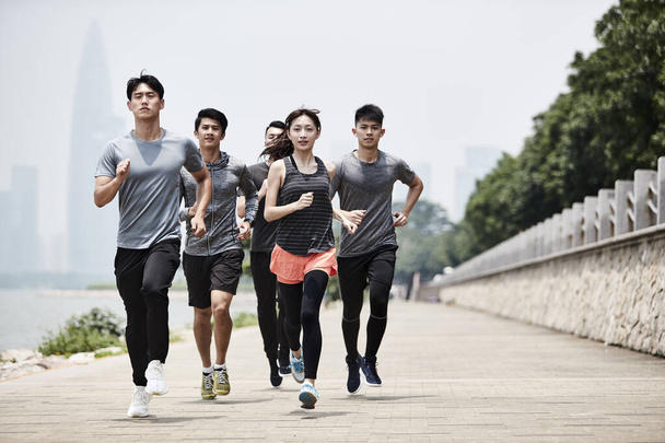 Gruppe von fünf jungen erwachsenen Männern und Frauen aus Asien beim Lauftraining im Freien - Foto, Bild