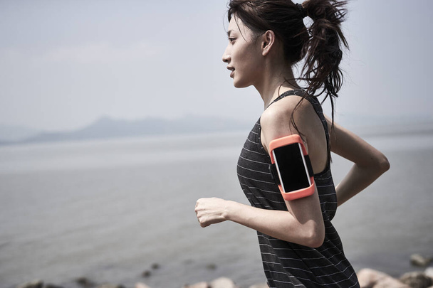 young asian adult woman running jogging outdoors by the sea, side view - Foto, Imagem