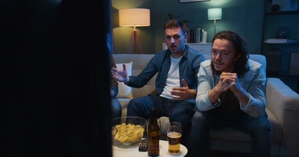Handsome Caucasian men football fans sitting on couch and watching football match late at night. Guys cheering and worrying for favorite team which missing goal and loosing in game. - Filmagem, Vídeo