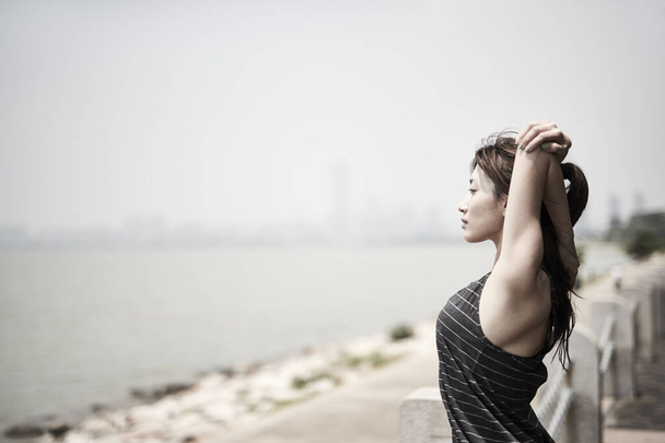 jong aziatisch volwassen vrouw stretching armen buiten door de zee, zijaanzicht - Foto, afbeelding