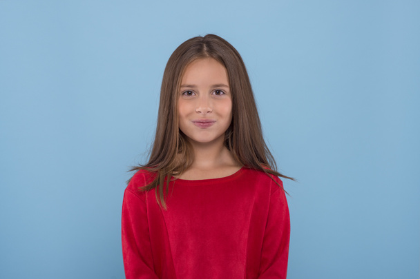 Waist up  portrait of a smiling young girl wearing red shirt against  blue background with copy space in studio.  - Foto, afbeelding