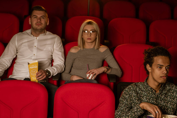 Image of laughing friends sitting in cinema watch film eating popcorn and drinking aerated sweet water. - Foto, Imagem