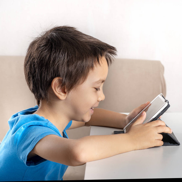 小さな笑顔の少年がタブレットでインターネットを閲覧のショット。現代の生活.   - 写真・画像