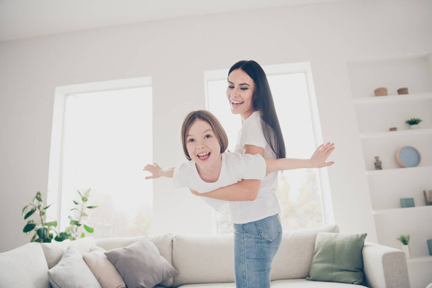 Photo of pretty funny little girl young charming mommy holding daughter hands having fun pretending airplane flight spend time weekend together indoors home house - Fotoğraf, Görsel