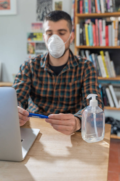 Coronavirus. Man working from home wearing protective mask. quarantine for coronavirus wearing protective mask. Working from home. Cleaning her hands with sanitizer gel. Thermometer fever inspection. - Zdjęcie, obraz