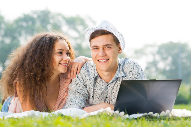 couple lying together in a park with laptop - Fotoğraf, Görsel