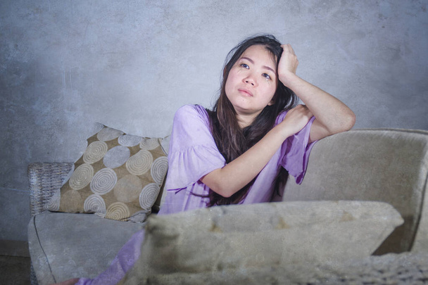 covid-19 virus home lockdown - dramatic portrait of young beautiful depressed and scared Asian Chinese woman lying sad and desperate on sofa couch feeling lonely and in panic about world crisis  - Foto, Bild