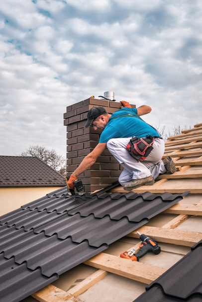 profesjonalny mistrz (dekarz) z elektrycznymi pokrywami śrubokrętów naprawia dach - Zdjęcie, obraz