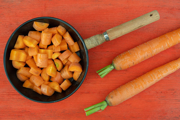 καρότα με πράσινα στελέχη σε κόκκινο ξύλινο τραπέζι, μαγείρεμα χορτοφαγικό πιάτο, φρέσκα λαχανικά από το αγρόκτημα - Φωτογραφία, εικόνα