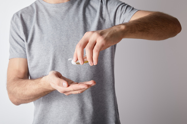 καλλιεργημένη άποψη του ανθρώπου που κρατά απολυμαντικό χεριών gel σε φιάλη σε γκρι φόντο - Φωτογραφία, εικόνα