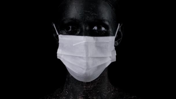 femme avec le visage de colord noir portant un masque médical sur fond blacvk pour se protéger contre le coronavirus. Nouveau coronavirus 2019-nCoV, pandémie
. - Séquence, vidéo